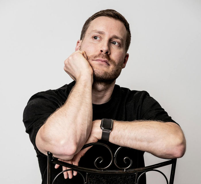 Man in black shirt looking thoughtful, leaning on chair, reflecting on cutting off parents after wedding plans conflict.