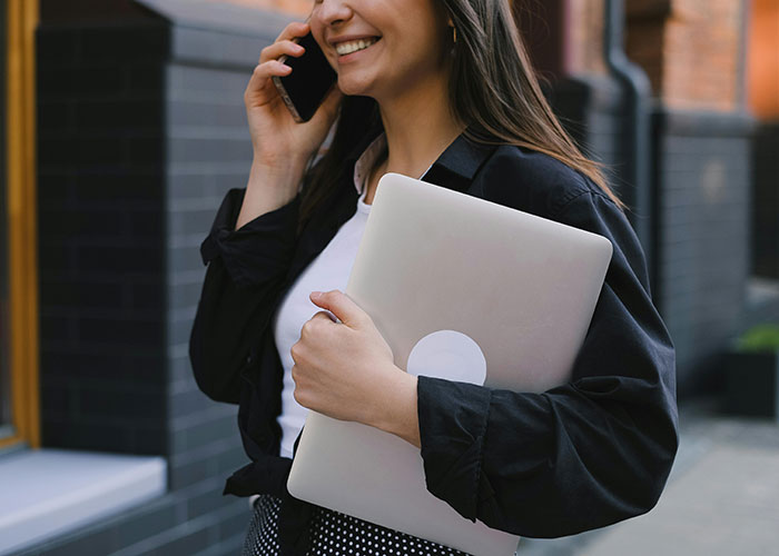 Woman holding a laptop and talking on a phone, illustrating phone dependence affecting family relationships. Woman holding a laptop and talking on a phone, illustrating phone dependence affecting family relationships.