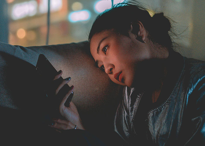 Woman looking intently at her phone in a dim room, illustrating phone dependence affecting family relationships.