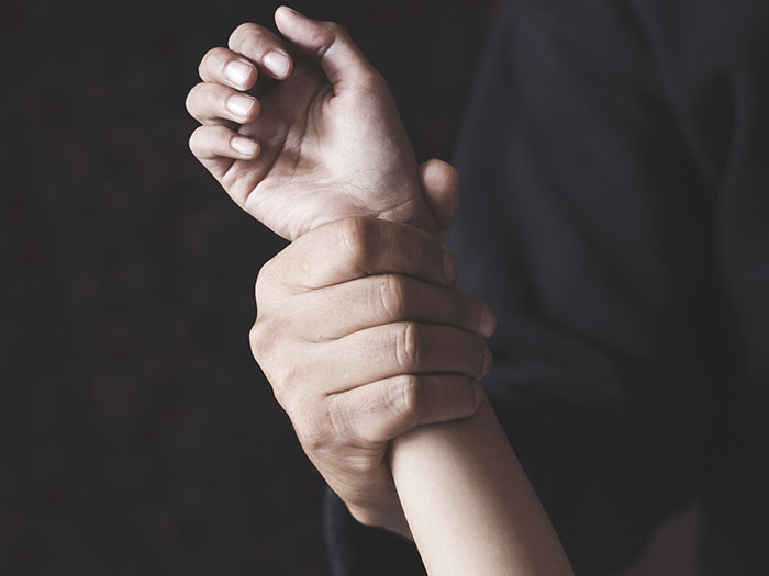 Close-up of hands gripping a wrist tightly, symbolizing kidnapping and rescue in a woods emergency.
