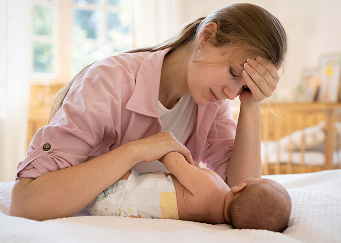 Stressed woman rethinks her relationship while holding her newborn baby alone in a softly lit bedroom setting.