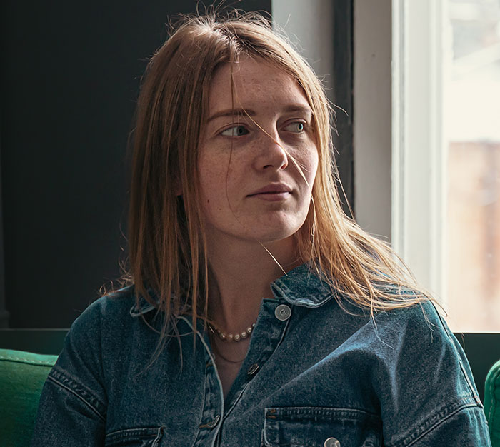 Young woman in a denim shirt looking out a window, illustrating mansplained moments with peak confidence and zero accuracy.