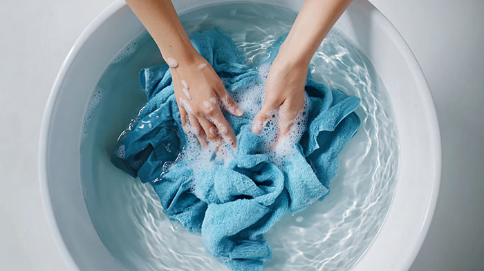 Hands washing a blue cloth in soapy water in a basin, illustrating mansplained confidence and zero accuracy concept.