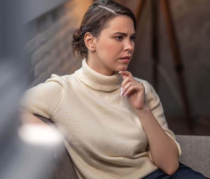 Woman wearing beige turtleneck looking skeptical and thoughtful while listening to mansplained conversation indoors