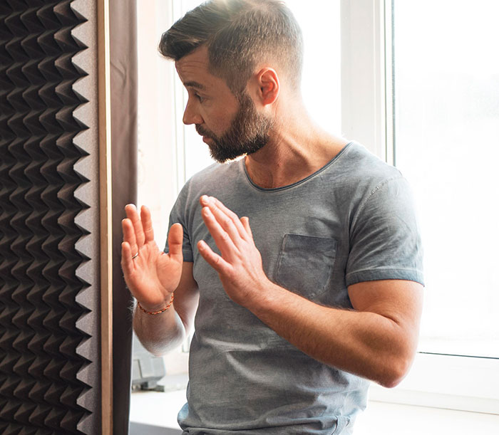 Man confidently mansplaining with raised hands near soundproof panel in a bright room, showing peak confidence and zero accuracy.