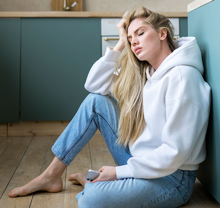 Woman sitting on floor looking frustrated while holding phone, illustrating mansplained moments with peak confidence and zero accuracy.