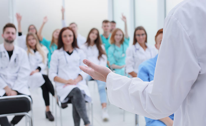 A confident man mansplaining to a group of women and men in white coats during a medical discussion.