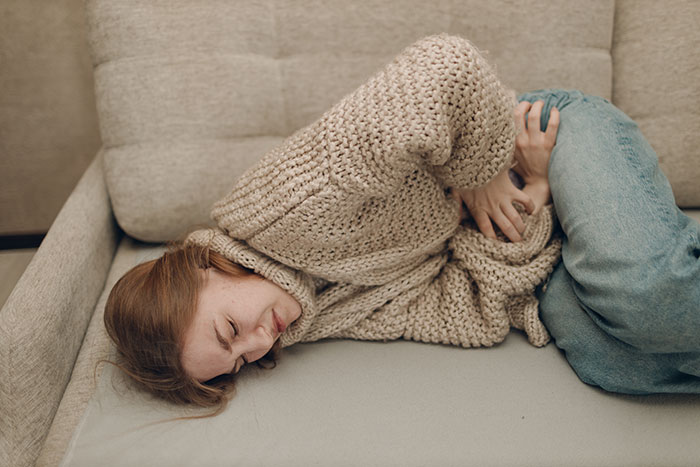 Woman lying on sofa in discomfort, illustrating the frustration often felt during mansplained conversations with peak confidence.