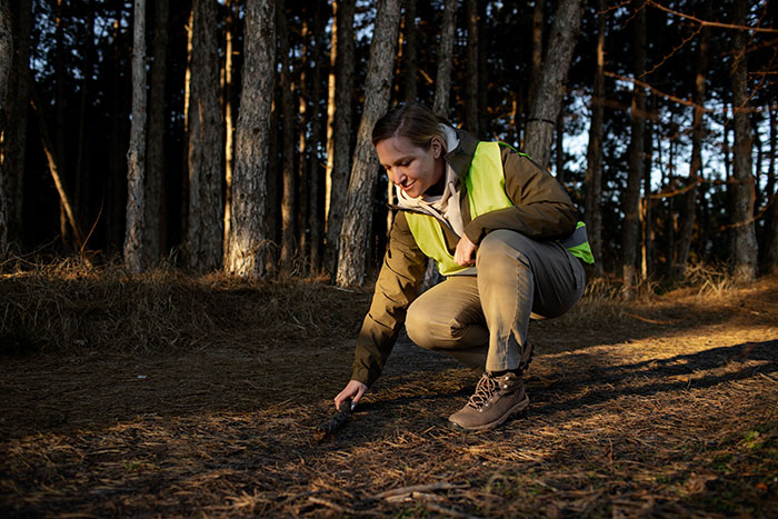 Woman wearing a safety vest crouching in the forest, illustrating mansplained moments with peak confidence and zero accuracy.