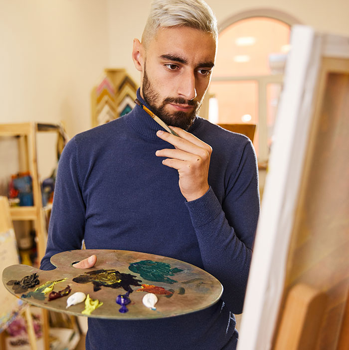 Man confidently mansplaining art techniques to woman while holding paint palette and brush in studio setting