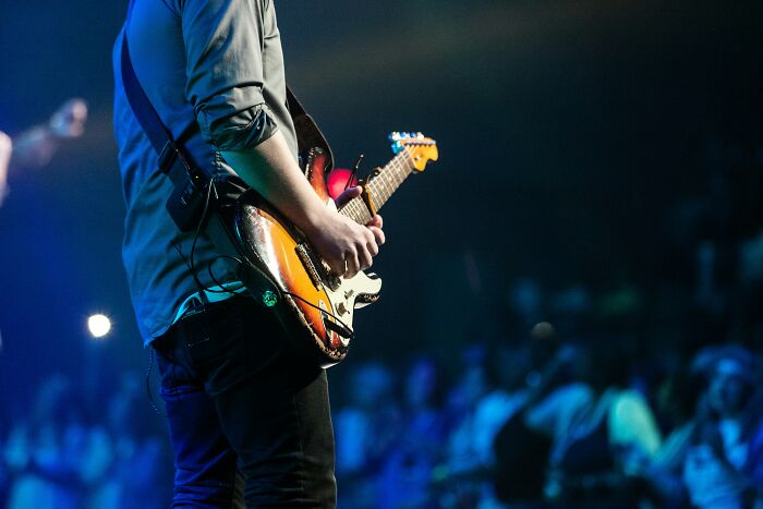 Musician playing an electric guitar on stage in front of a crowd, highlighting once-famous regular job in entertainment.