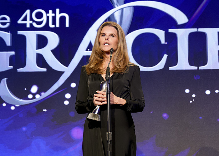 Maria Shriver speaking at a podium during an awards event, addressing topics related to Kennedy Center renaming.