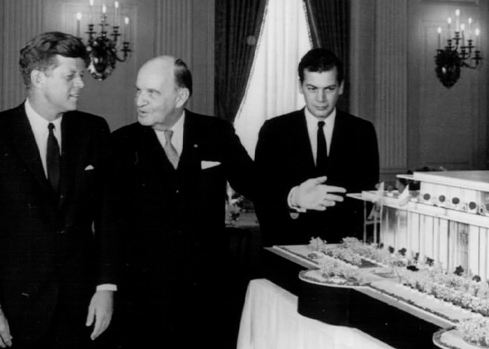 Black and white photo showing three men in suits examining a detailed architectural model of the Kennedy Center.