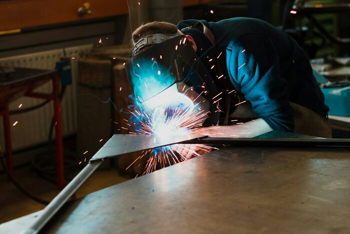 Person wearing protective gear welding metal in a workshop, demonstrating incredible minds and genius without a degree.