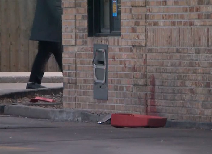 Drive-thru accident scene at McDonald&rsquo;s with damaged items and a person walking past a brick wall near the order machine.
