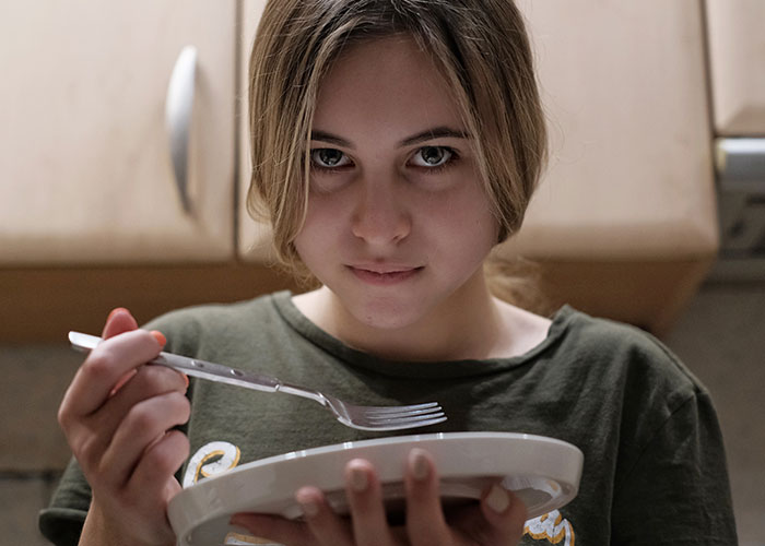 Young woman threatening sister's life, holding plate and fork in kitchen, parents hope for Christmas family reunion. Young woman threatening sister's life, holding plate and fork in kitchen, parents hope for Christmas family reunion.
