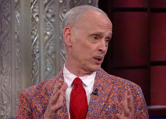 Man in colorful blazer and red tie sharing stories about famous people they've met on a talk show set.