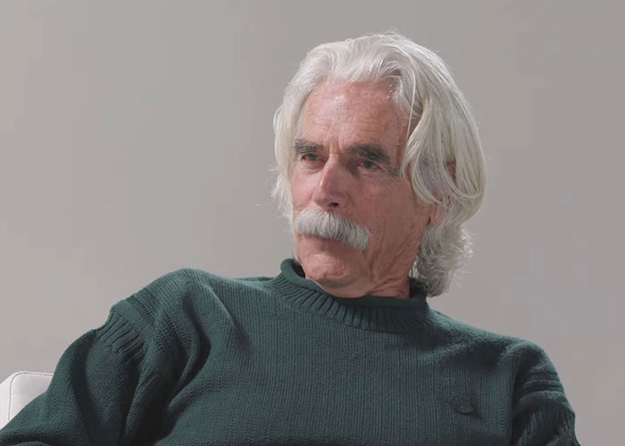 Elderly man with white hair and mustache wearing a green sweater sharing stories about famous people they've met.