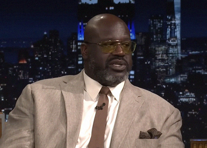 Man in beige suit and tinted glasses sharing stories about famous people they've met on a late-night talk show.