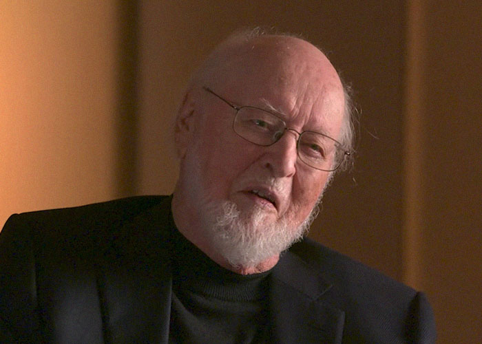 Elderly man with glasses and a white beard sharing stories about famous people they've met in a warm setting