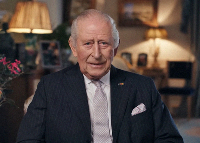 Elderly man in a dark suit and tie sitting indoors, sharing stories about famous people they've met and their personalities.