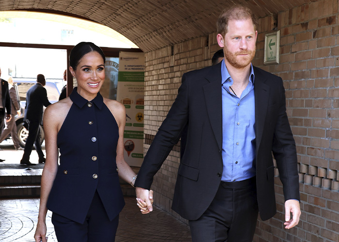 Meghan Markle and Prince Harry holding hands, walking together in a public outdoor setting with smiles. Meghan Markle and Prince Harry holding hands, walking together in a public outdoor setting with smiles.