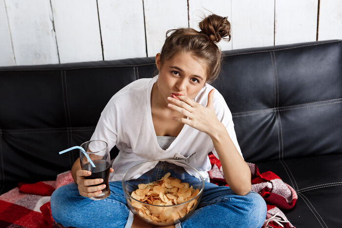 Young woman sitting on couch eating chips and holding a drink, illustrating insights men share about women in relationships.