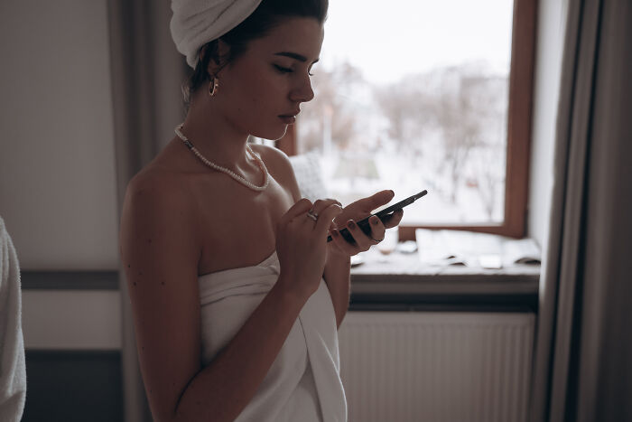 Woman wrapped in towel using smartphone indoors near window, reflecting on marriage and relationships insights shared by men.