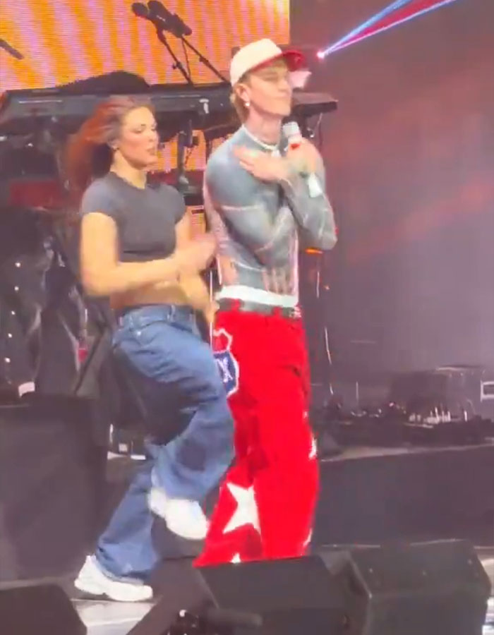 Machine Gun Kelly dancing on stage with a female dancer in casual and colorful outfits during a live performance. Machine Gun Kelly dancing on stage with a female dancer in casual and colorful outfits during a live performance.