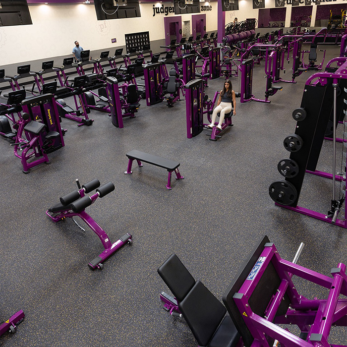 Interior view of a Miami gym with purple exercise machines and a few people working out in the spacious area.