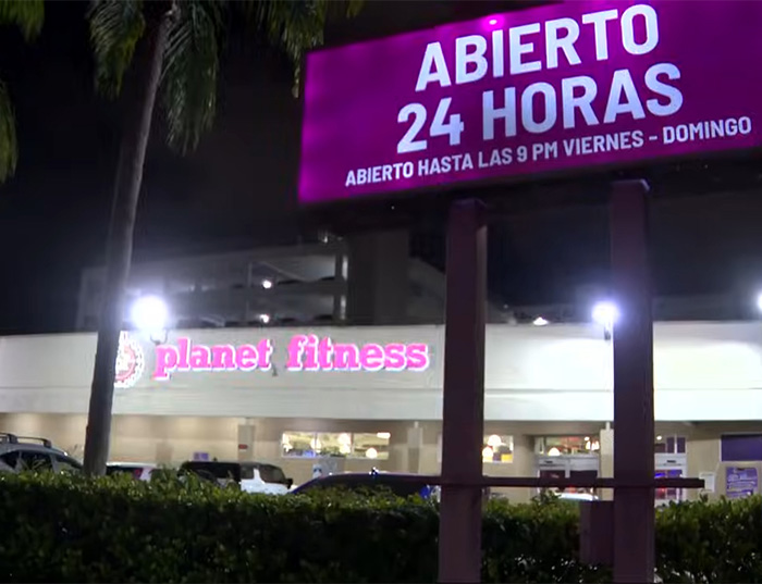 Planet Fitness gym in Miami at night with illuminated signs showing 24-hour service and parking lot visible.