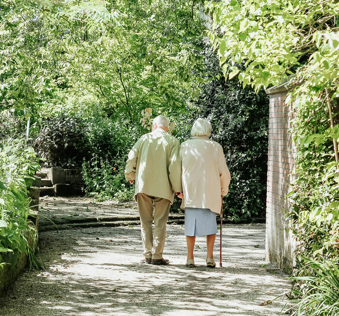 Elderly couple walking together in a sunlit garden path, symbolizing times people became rich out of nowhere.