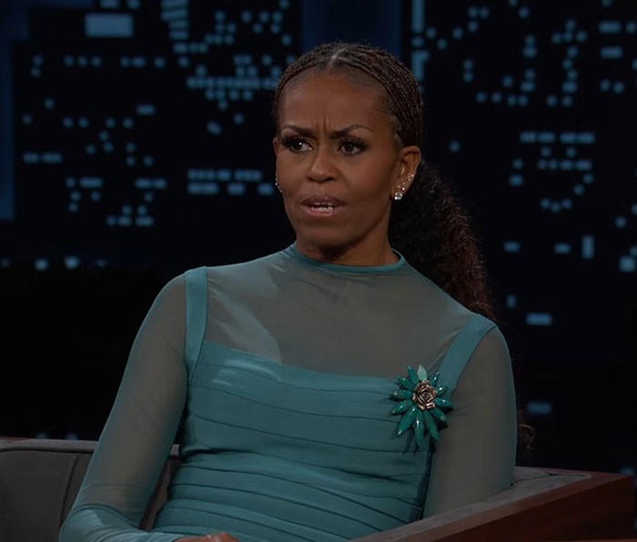Michelle Obama speaking seriously during a televised interview with a cityscape background at night. Michelle Obama speaking seriously during a televised interview with a cityscape background at night.
