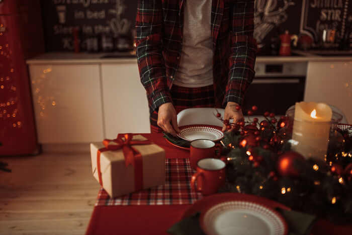 Person setting a holiday table with gift box and festive decorations, hinting relationship insights expert warns about. Person setting a holiday table with gift box and festive decorations, hinting relationship insights expert warns about.