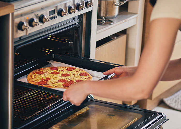 Woman reheating pizza leftovers in kitchen oven, preparing food for family during holiday visit unannounced at Christmas.