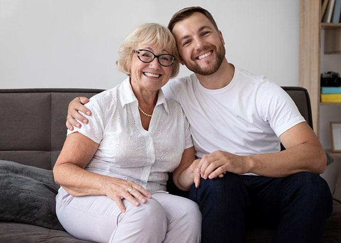 Smiling young man and older woman sitting close on sofa, representing woman reheats pizza leftovers for MIL during Xmas visit. Smiling young man and older woman sitting close on sofa, representing woman reheats pizza leftovers for MIL during Xmas visit.
