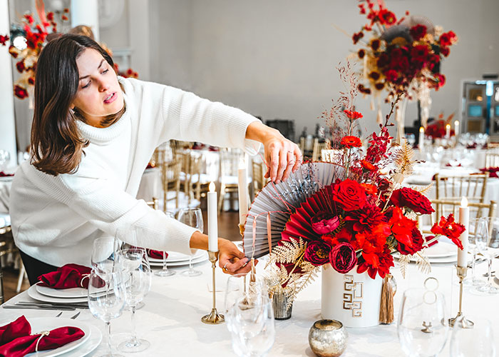 Woman adjusting red floral centerpiece at wedding venue, highlighting mil demands and venue changes stuck in storm delays