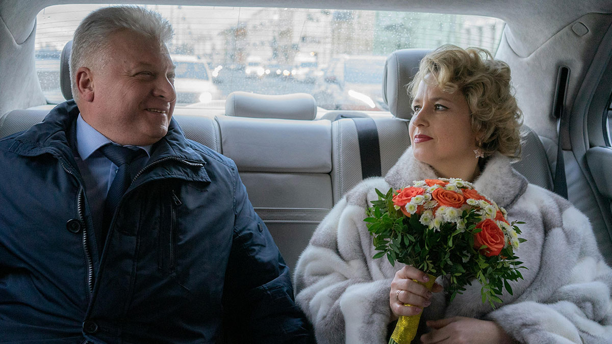 Military man and bride holding a bouquet, sitting in a car discussing wedding venue changes stuck in a storm.
