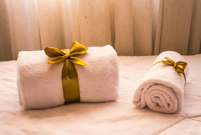 Two rolled white towels tied with gold ribbons, placed on a bed, symbolizing holiday gift wrapping traditions. Two rolled white towels tied with gold ribbons, placed on a bed, symbolizing holiday gift wrapping traditions.