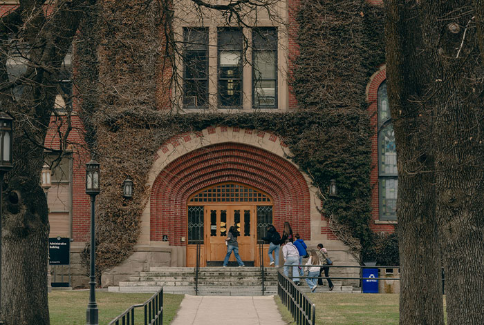Students walking towards a large brick building with ivy, illustrating tension as unhinged MIL loses her job in the story. Students walking towards a large brick building with ivy, illustrating tension as unhinged MIL loses her job in the story.