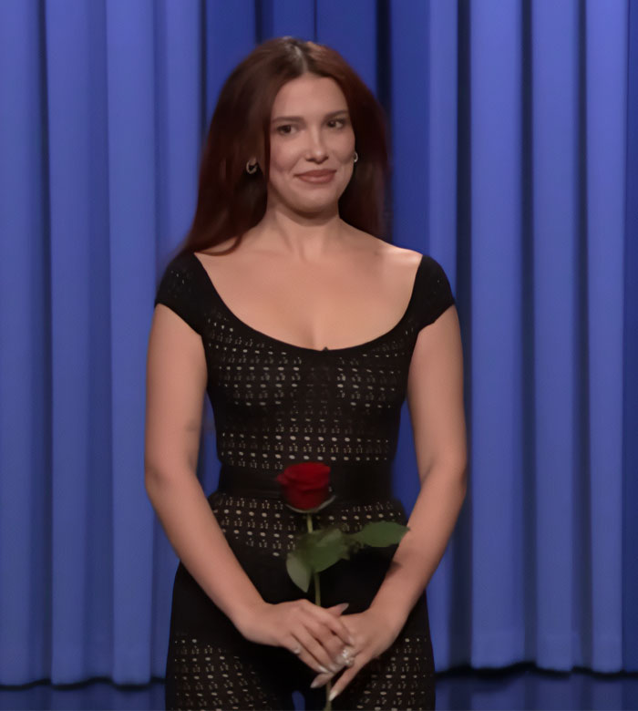 Actress in a sheer black outfit holding a red rose, highlighted in a studio setting with a blue curtain backdrop. Actress in a sheer black outfit holding a red rose, highlighted in a studio setting with a blue curtain backdrop.