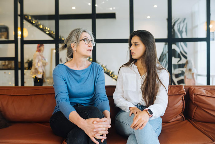 Older woman and younger woman sitting on a couch in a modern room, appearing tense during a conversation about bride&rsquo;s parents tantrums.