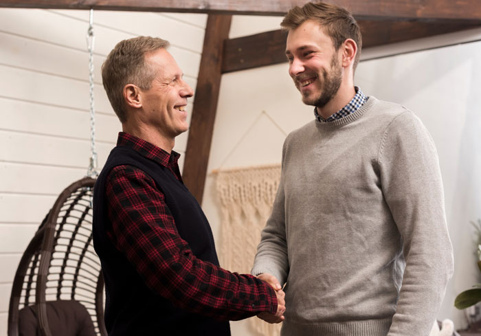 Two men shaking hands indoors, illustrating bride&rsquo;s parents amid wedding family tensions and confrontations.