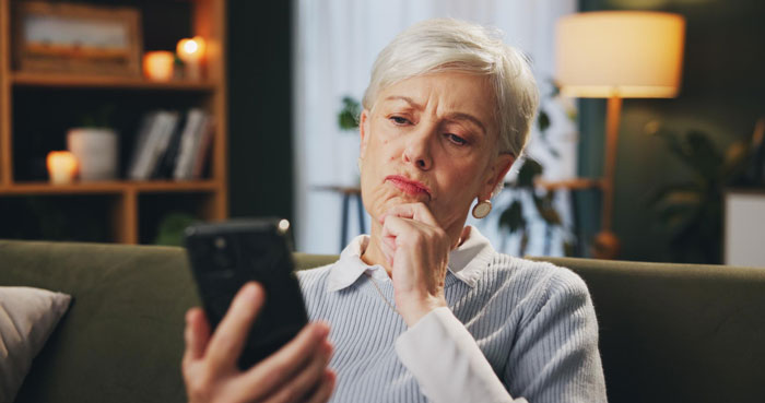 Older woman looking upset and frustrated while holding a phone, depicting mom rage over forgotten birthday and labor timing. Older woman looking upset and frustrated while holding a phone, depicting mom rage over forgotten birthday and labor timing.