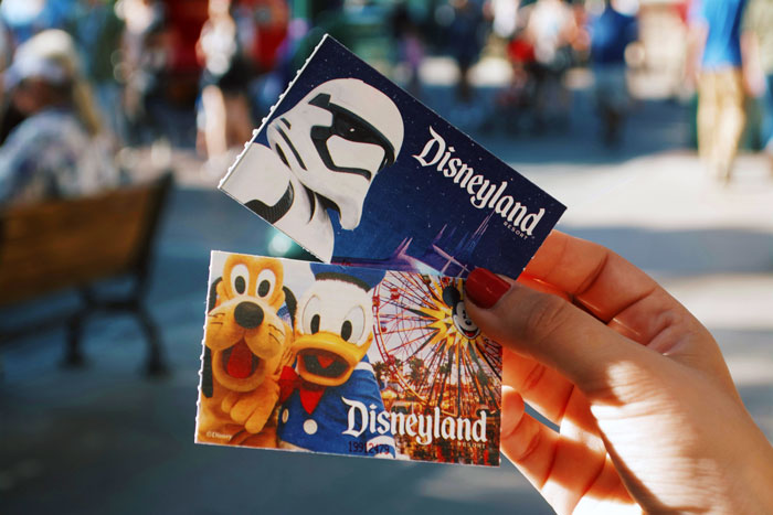 Hand holding Disneyland tickets featuring Star Wars and classic characters representing a Disney dream with hidden debt and guilt.