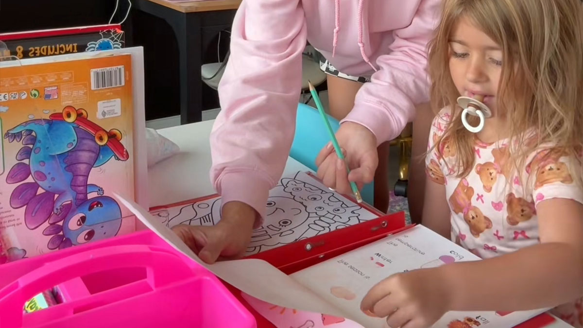 Child using a coloring book with adult assistance in a homeschool setting raising parenting choice questions.