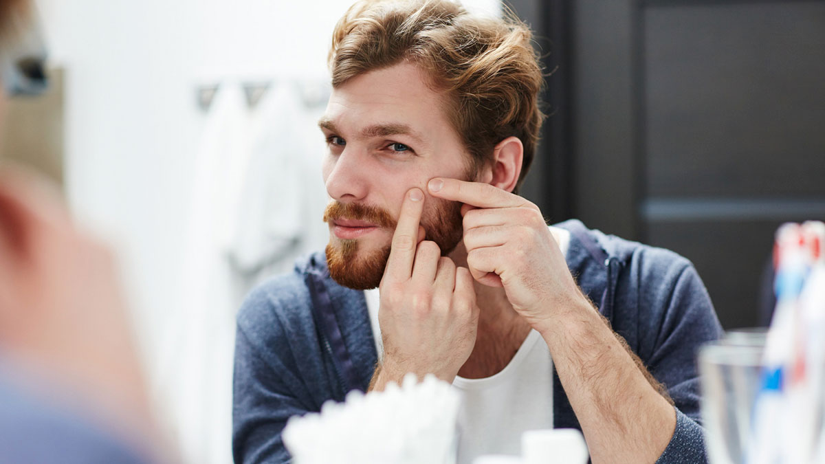 Young man squeezing face blemish in front of mirror during embarrassing moments people were blessed to see others do