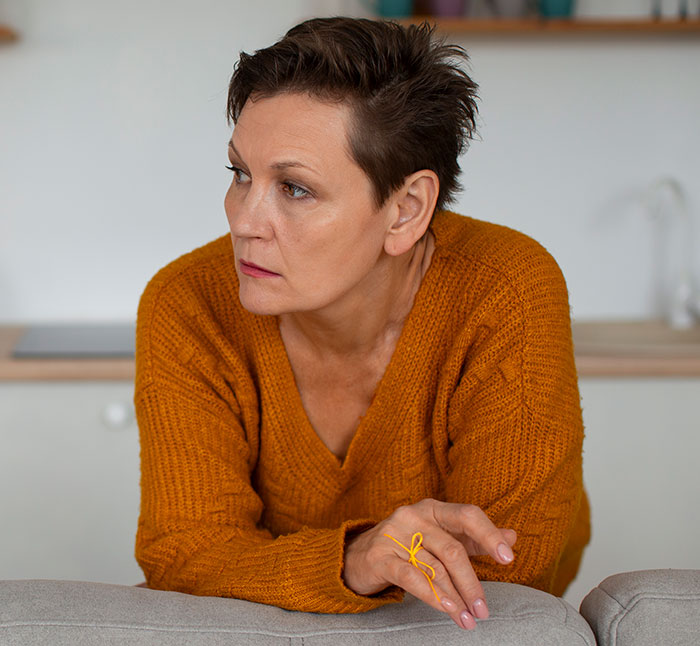 Woman in orange sweater looking concerned, illustrating a mom accused of embarrassing son’s girlfriend in a home setting. Woman in orange sweater looking concerned, illustrating a mom accused of embarrassing son’s girlfriend in a home setting.