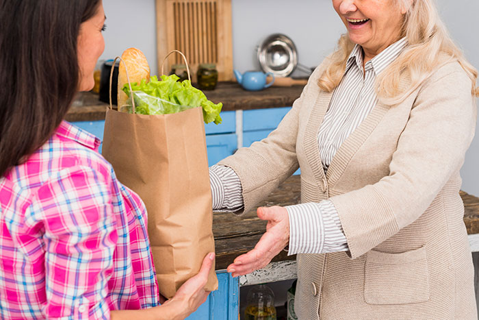 Couple hosting expensive Thanksgiving dinner exchanging groceries in a cozy kitchen setting, smiling and interacting warmly.