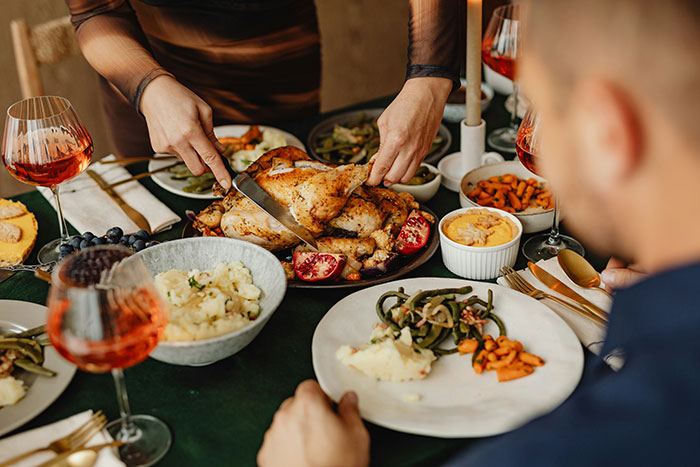 Couple hosting an expensive Thanksgiving dinner with roasted turkey and traditional side dishes on a festive table.